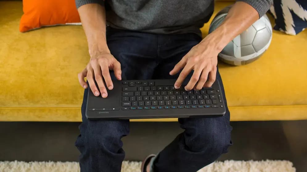 A man sitting on a coach and working with a keyboard on the knees